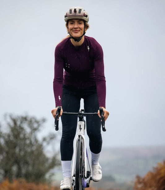 Front-view-of-a-smiling-female- cyclist-riding-a-road-bike-uphill- wearing-a-burgundy-long-sleeve- cycling-jersey-and-black-leggings