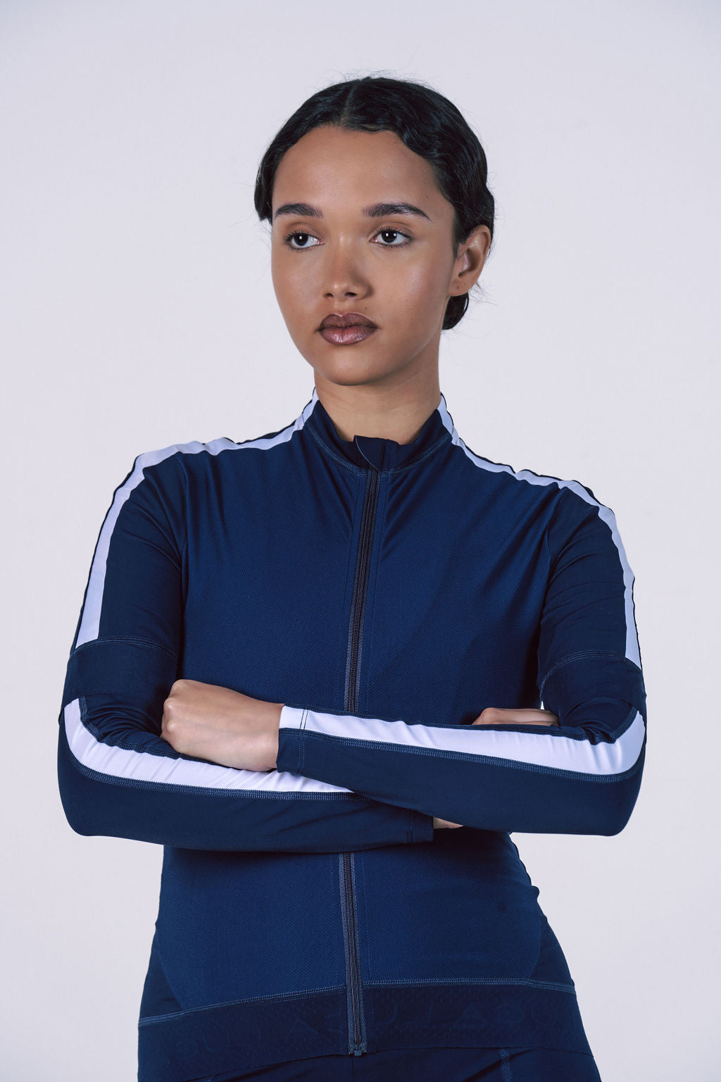 Studio-close-up-of-a-woman- wearing-a-navy-blue-athletic-zip-up-jacket-with-white-stripes-running-down-the- sleeves-She-is-standing-with-her-arms-crossed-This-jacket-is-ideal-for- women's-track-jackets-running-warm-up-gear-cycling-wear-apparel