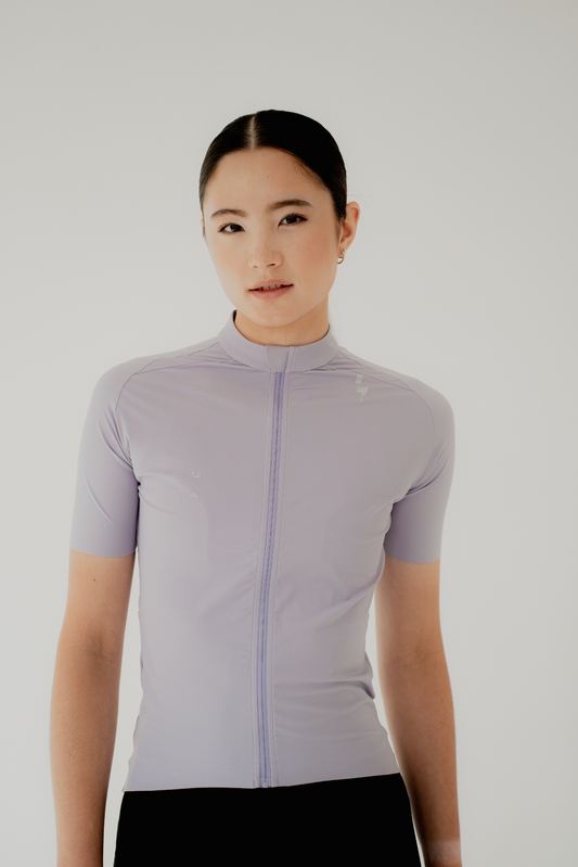 Woman-zipping-up-a-light-purple-jacket-over-a-black-sporty-one-piece-garment-with-the-LUCA-logo-printed-on-the-chest