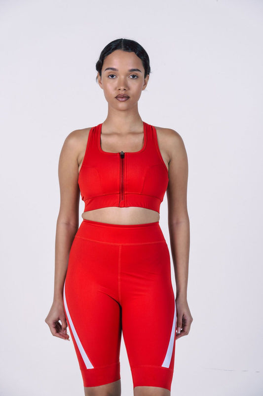 A-studio-shot-of-a-woman-modeling -an-athletic-two-piece-outfit-against-a-plain-white-background- She-is-wearing-a-bright-red-high-support-sports-bra-top-with-wide- shoulder-straps-and-a-black-front- zipper-She-is-also-wearing-matching-red-high-waisted-cycling- shorts-that-feature-white-graphic- stripes-curving-up-from-the-hem-on-the-sides-of-the-legs