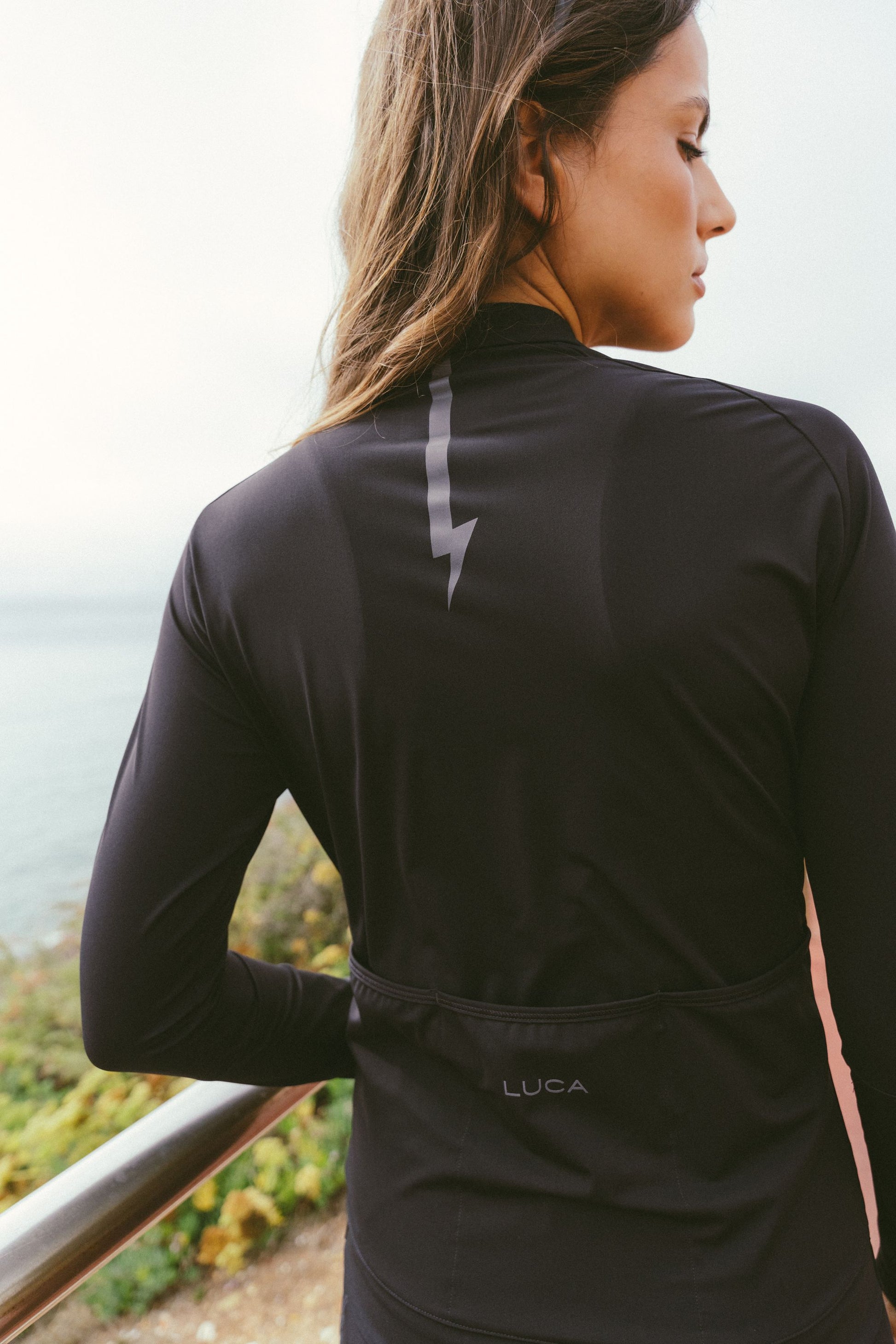 Black-view-of-the-model-wearing-the-black-Horizon-jersey-highlighting-the-large-reflective-lighting-bolt-graphic-down-the-spine-for-safety-and-style-and-the-LUCA-text-logo-above-the-rear-pockets