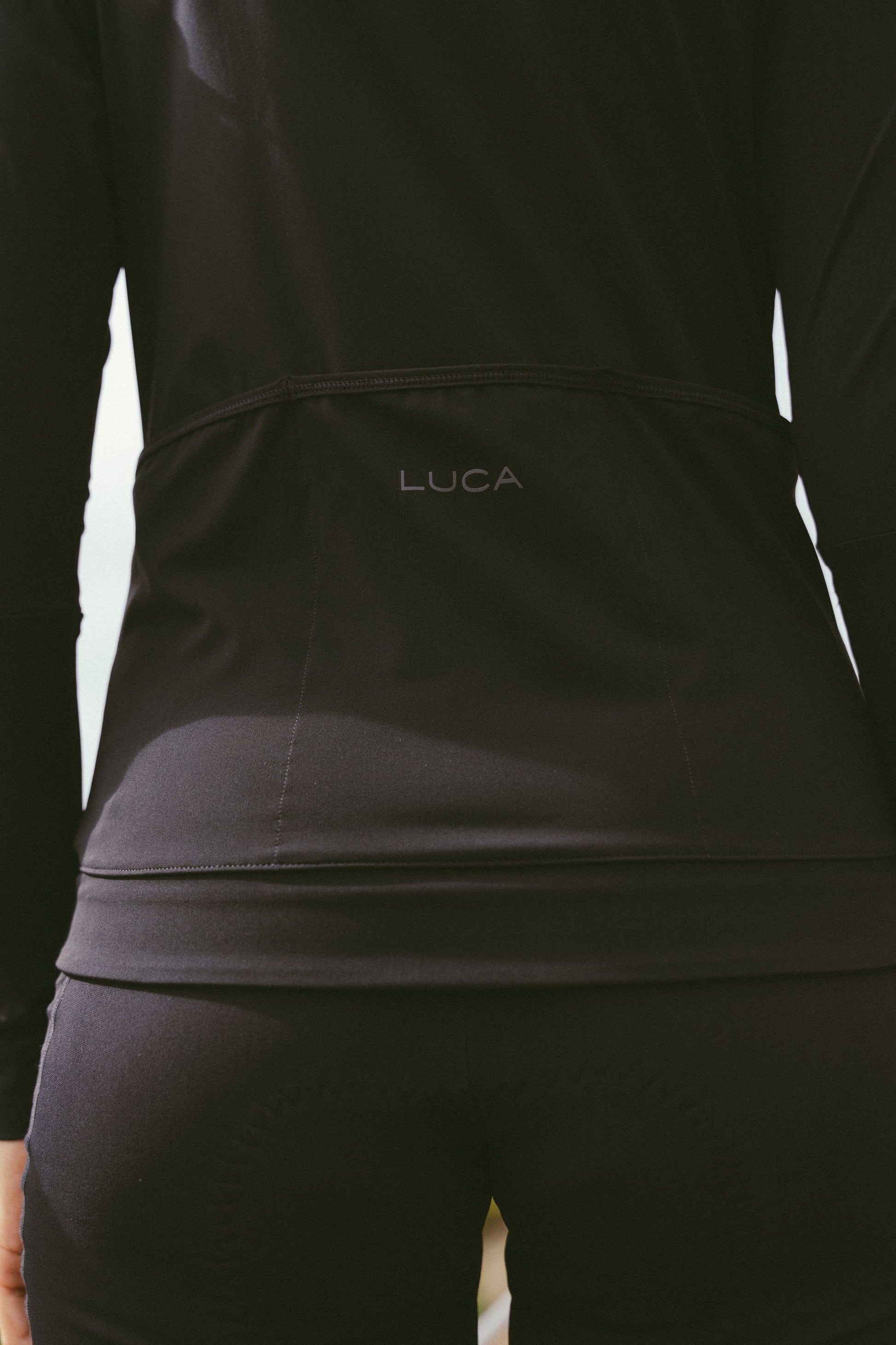 Close-up-of-the-lower-back-of-the-black-Horizon-jersey-showing-the-subtle-LUCA-branding-positioned-above-the-stitched-seam-of-the-three-reinforced-rear-storage-pockets