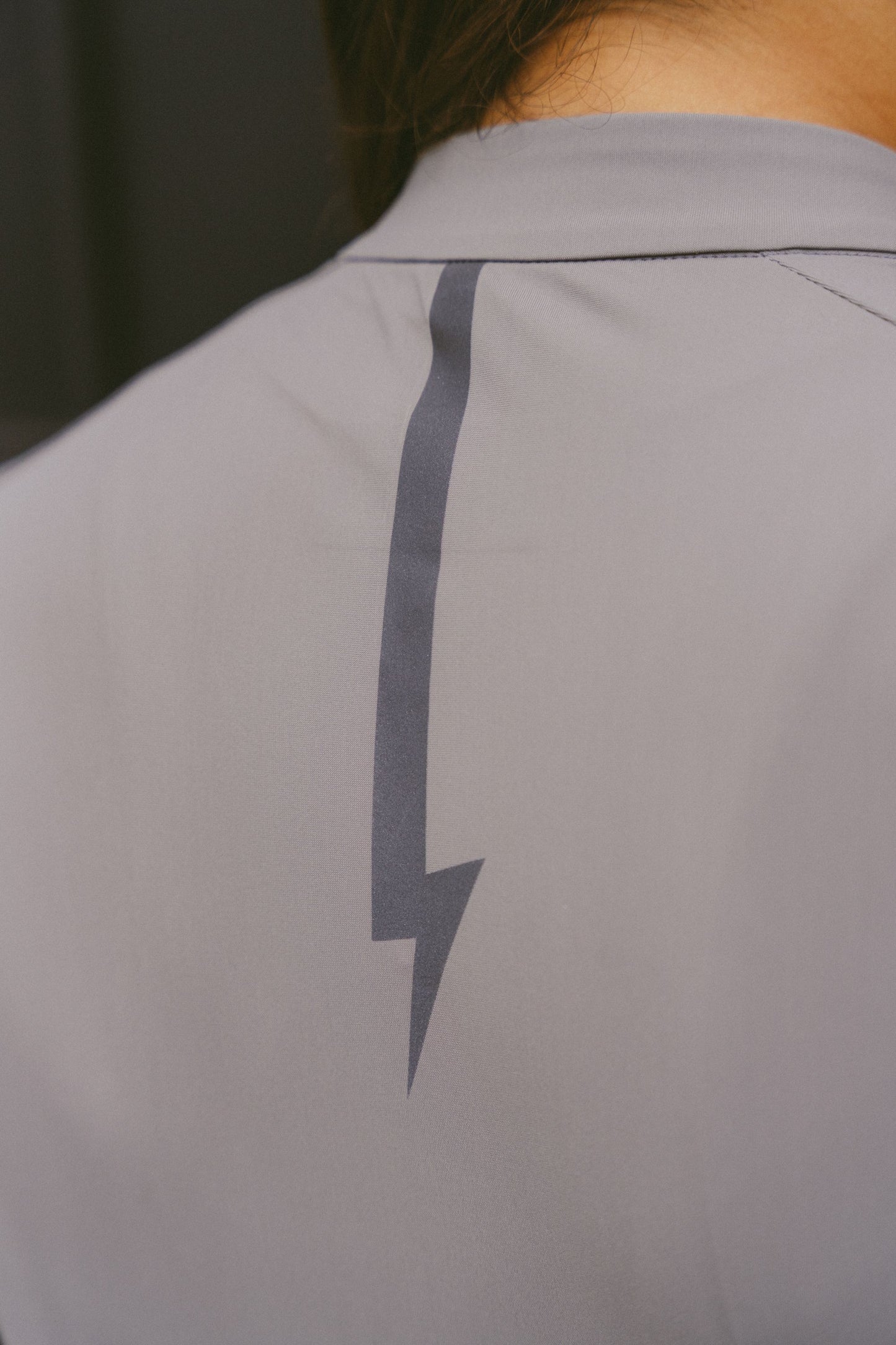 Close-up-of-the-reflective-lighting-bolt-on-the-upper-back-of-the-gray-Harizon-long-sleeve-athletic-jersey-designed-for-enhanced-visibility-and-signature-branding