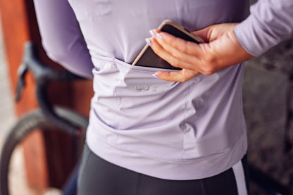 Close-up-of-a-hand-placing-a-smartphone-into-the-back-pocket-of-the-lilac-athltic-jersey-demonstrating-the-jersey-convenient-and-secure-storae-for-essentials-while-riding