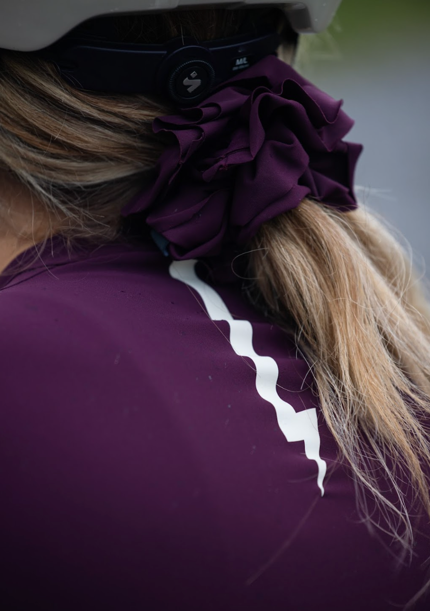 Close-up-of-a-ruffled-dark-purple- scrunchie-and-a-white-stripe-detail- on-a-purple-cycling-jersey