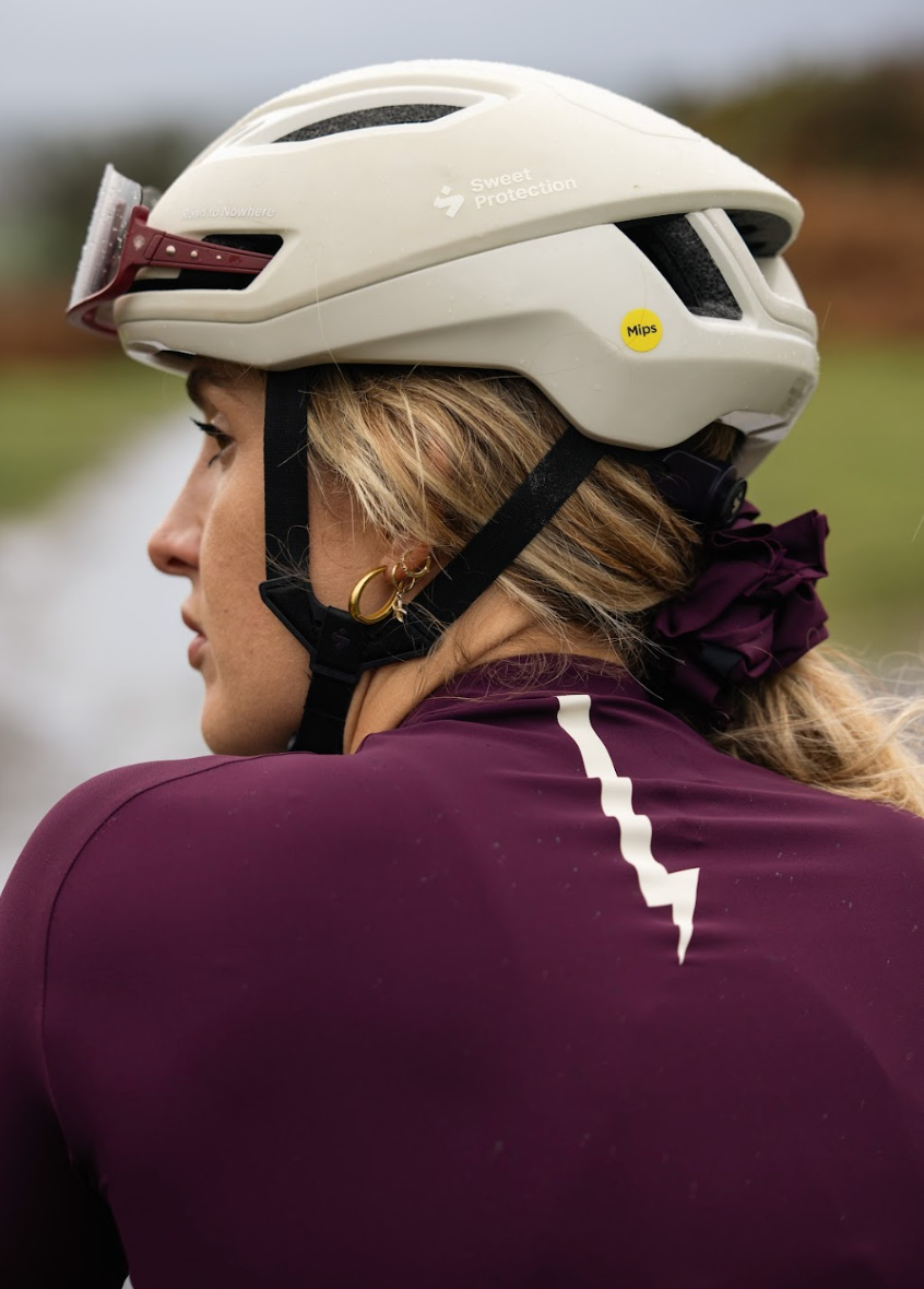 Woman-wearing-a-Sweet-Protection-MIPS-cycling-helmet-and-a-dark-purple-jersey-with-a- white-lightning-bolt-sign