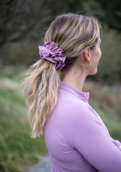 Side-view-of-a-woman-outdoors- wearing-a-light-purple-top-with-her- blonde-hair-tied-back-in-a-ponytail- using-a-large-ruffled-dark-purple- scrunchie