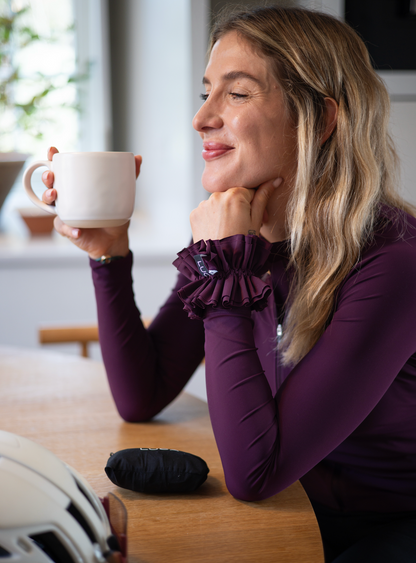 Woman-relaxing-and-drinking-coffee-while-wearing-a-purple-long-sleeve-top-with-ruffled-cuffs