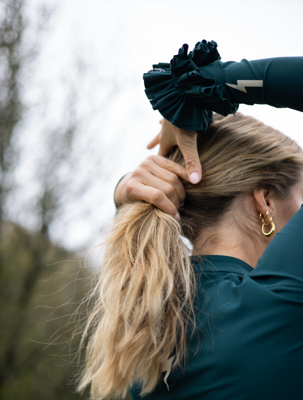 Close-up-showing-a-gold-hoop- earring-Uplift-Scrunchie-Teal-and-a- green-athletic-top-with-a-lightning- bolt-sign-on-the-sleeve