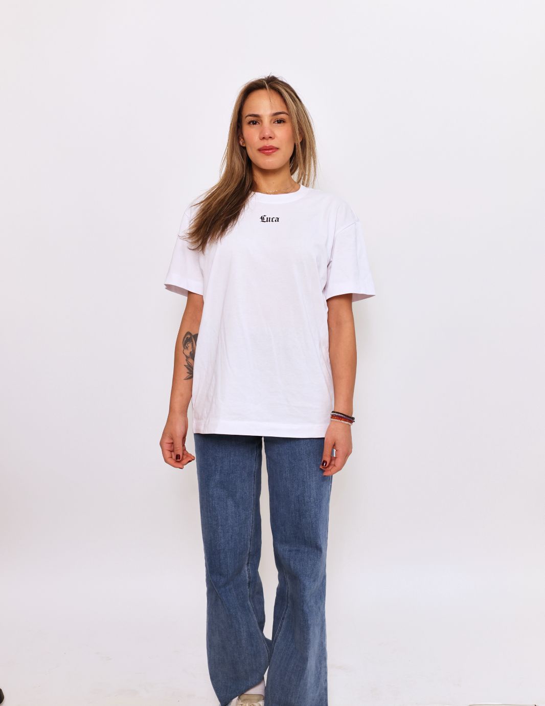 Front-view-of-a-woman-wearing-an- oversized-white-t-shirt-featuring-the-word-"Luca"-printed-in-a-small- black-gothic-font-on-the-chest-She- is-also-wearing-blue-jeans